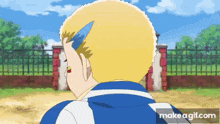 a man with blonde hair is standing in front of a fence and a brick wall .