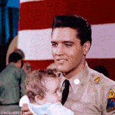 a man in a military uniform is holding a baby in front of a flag