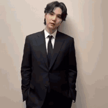 a young man in a suit and tie is standing in front of a white wall .