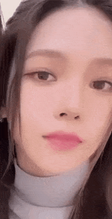 a close up of a woman 's face wearing a white turtleneck and pink lipstick .