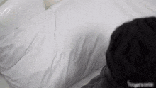 a person wearing a black supreme hat is laying on a bed