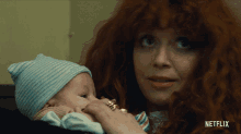 a woman with red hair is holding a baby in her arms with netflix written on the bottom
