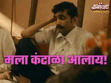 a man with a mustache is sitting in front of a sign that says " mala kadhaa allaya "