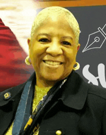 a woman is smiling for the camera while wearing a black jacket and earrings .