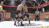 two men are fighting in a wrestling ring with a referee in the background .