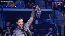 a wrestler is holding up a championship belt in front of a crowd sponsored by peacock