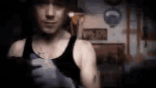 a man in a black tank top is standing in a dark room holding a knife .