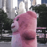 a large pink teddy bear stands in front of a city skyline