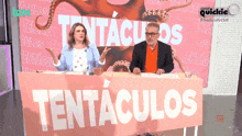 a man and a woman sit at a table with a tentaculos sign in front of them