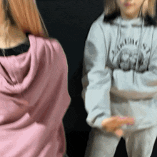 a girl in a pink hoodie is standing next to another girl in a gray hoodie