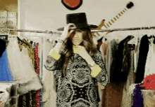 a woman wearing a top hat is standing in front of a guitar hanging on a rack