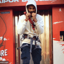 a man wearing a hoodie and a harness stands in front of a sign that says bungee