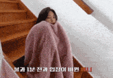 a woman wrapped in a pink blanket is sitting on stairs