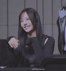 a woman with long black hair is smiling in front of an oldman sunny sign