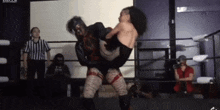 two women are wrestling in a wrestling ring while a referee watches .