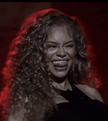 a woman with curly hair is laughing with her mouth open