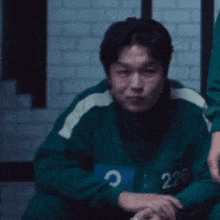 a man in a green sweater with the number 226 on it is sitting on the floor in a dark room .