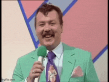 a man in a green suit is holding a microphone and smiling .