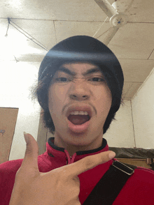 a young man wearing a black beanie and a red sweater makes a funny face