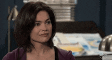 a woman in a purple sweater is sitting in front of a desk with a lamp .