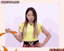 a girl in a yellow crop top is standing with her hands on her hips and the words honeycam.org above her