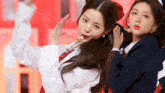 two girls in school uniforms are dancing on a stage . one of the girls is wearing a red bow in her hair .