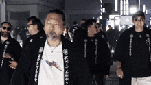 a group of men are walking down a street with one wearing a shirt with chinese writing on it