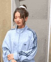 a woman wearing a blue adidas jacket is standing in front of a door