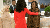 a woman in a red dress is hugging another woman in a leopard print jacket