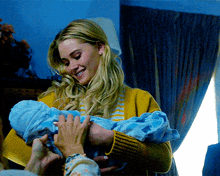 a woman in a yellow sweater is holding a blue baby