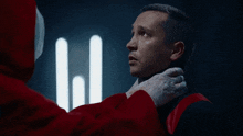 a man in a red hoodie is holding another man 's neck in a dark room
