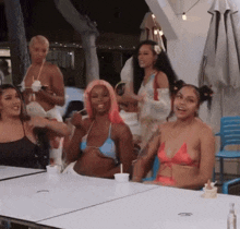 a group of women in bikinis are sitting at a table with drinks