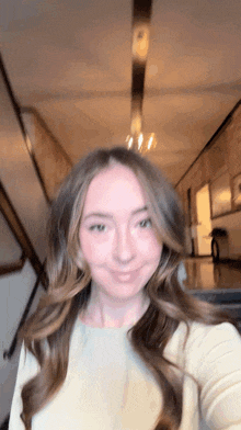 a woman with long brown hair is taking a selfie in a hallway .