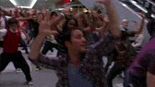 a group of people are dancing in a mall and one of them is wearing a plaid shirt
