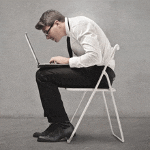 a man in a suit is sitting in a folding chair using a laptop