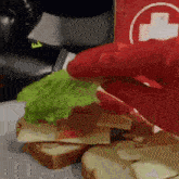 a person in a red glove is eating a sandwich with lettuce , cheese and meat .