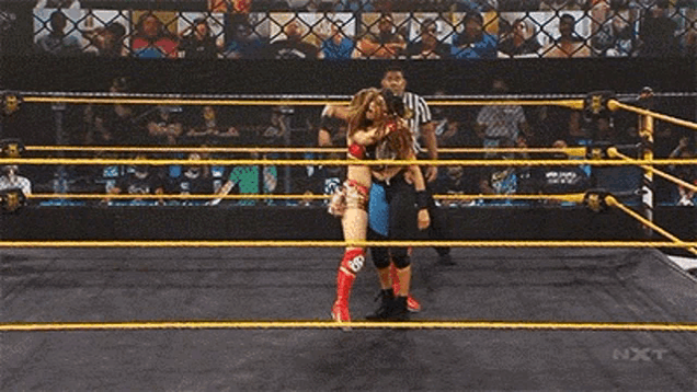 two women are wrestling in a wrestling ring with a referee in the background .
