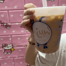 a person is holding a cup of milk tea with a straw in front of a hello kitty wall .