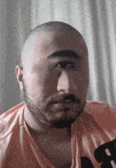 a man with a beard is wearing a pink shirt with the letter b on the front