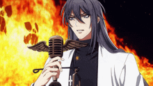 a man with long hair is holding a microphone with wings on it and a fire in the background