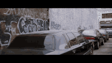 cars are parked in front of a brick wall that has graffiti on it