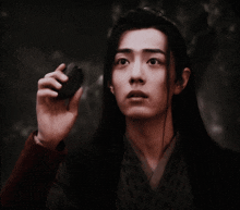 a man with long black hair is holding something in his hand .