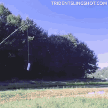 a slingshot is being thrown in a field with the website tridentslingshot.com visible