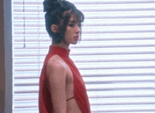a woman is standing in front of a window wearing a red dress .