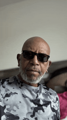 a man wearing sunglasses and a camouflage shirt looks at the camera