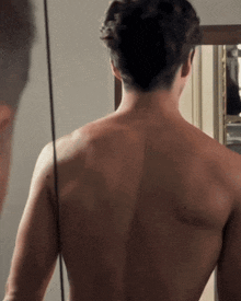 a man without a shirt is looking at his back in a mirror