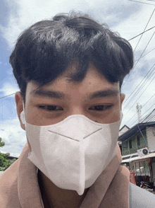 a young man wearing a white face mask looks at the camera with a building in the background