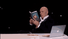a man is sitting at a table with a laptop and throwing a trash can .