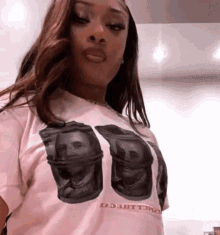 a woman wearing a pink t-shirt with a picture of a dollar bill on it is taking a selfie .