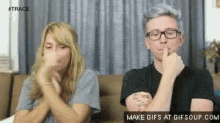 a man and a woman are sitting on a couch and the man is holding his finger to his mouth .